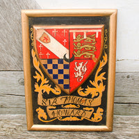 Framed coat of arms with 'Sir Thomas Howard' on a wooden surface