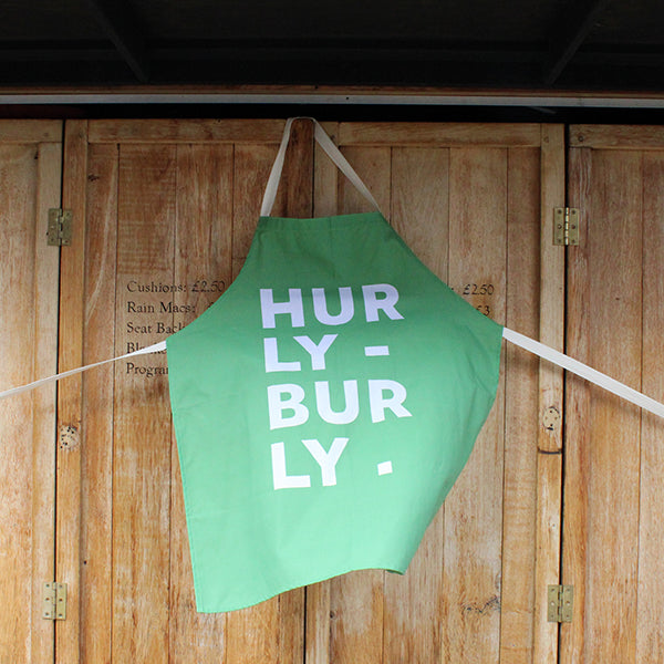 
                  
                    Pale green cotton apron with natural cotton straps, featuring white typographic text
                  
                