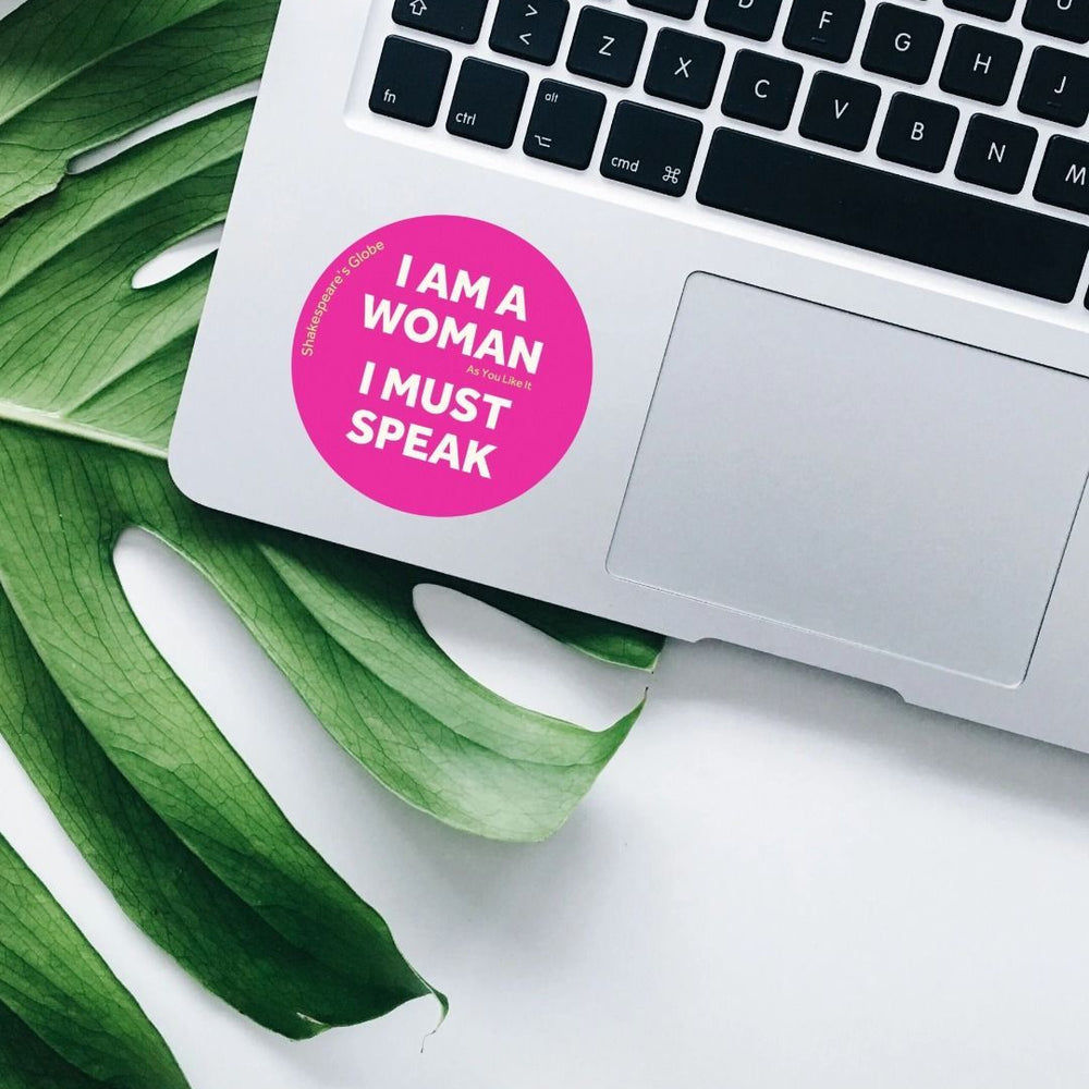 Circular fuchsia pink sticker with white text, stuck on a silver laptop with a monstera leaf behind