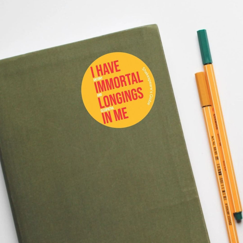 Yellow circular sticker with red and white graphic text on it, stuck to a notebook with pens sitting aside