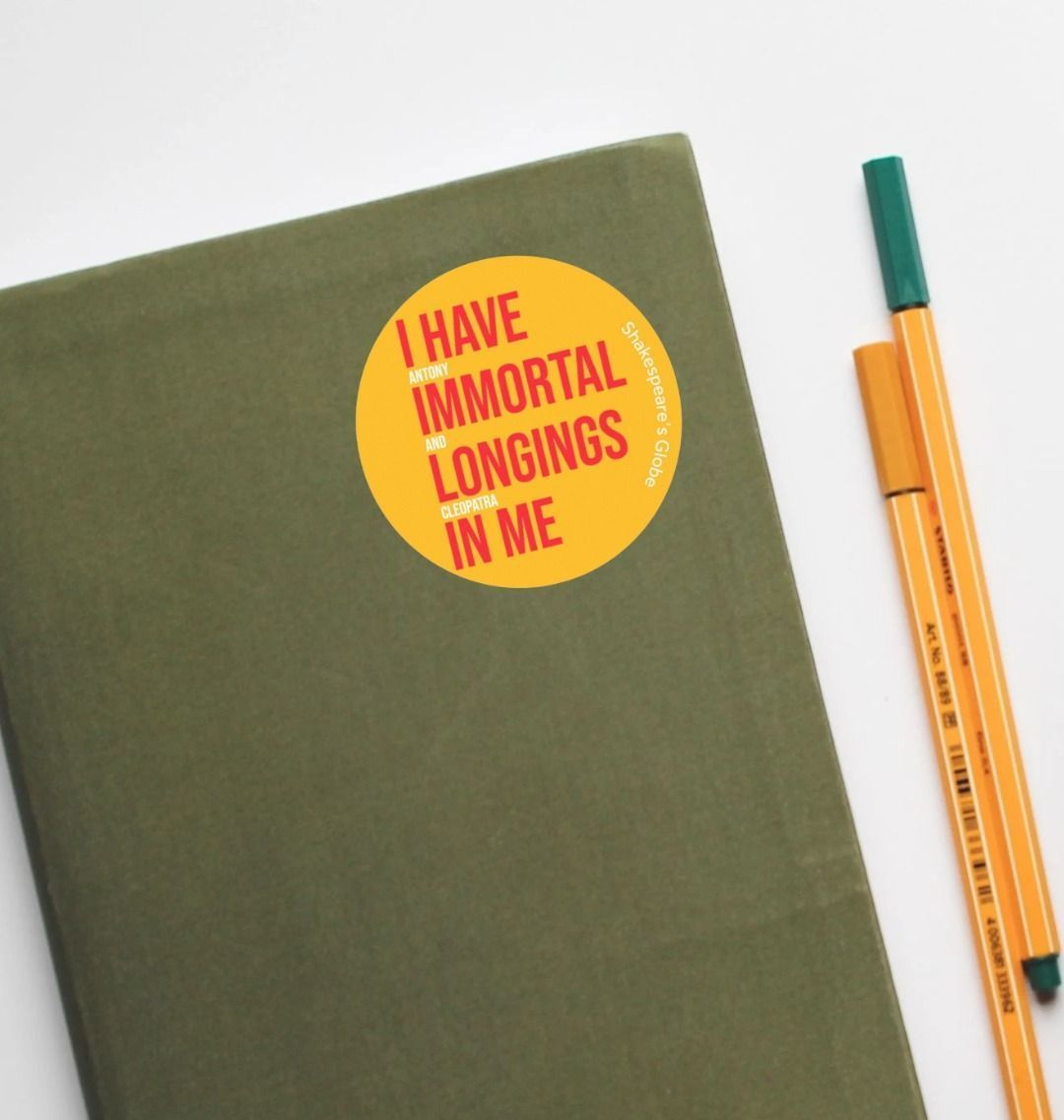 Yellow circular sticker with red and white graphic text on it, stuck to a notebook with pens sitting aside