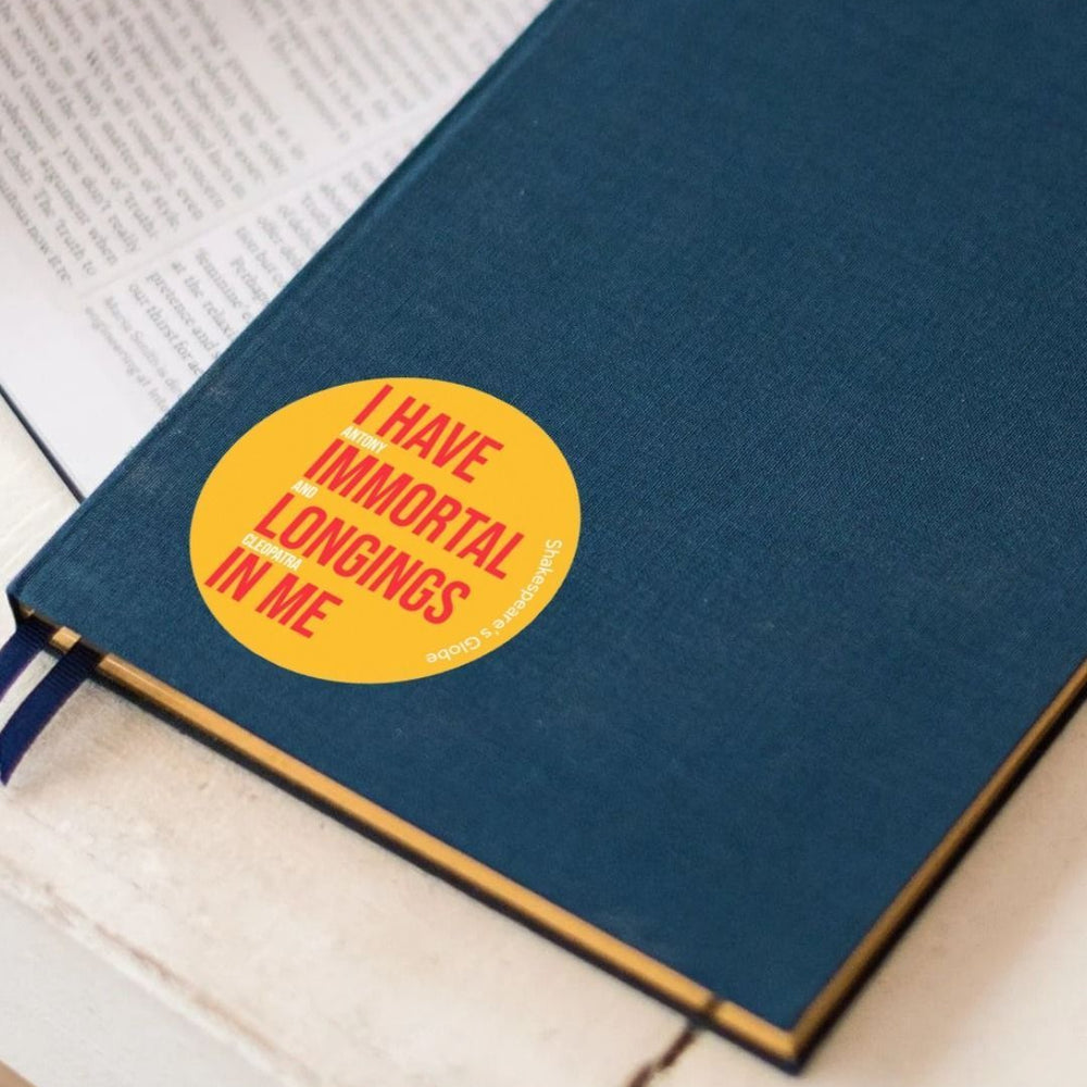 Yellow circular sticker with red and white graphic text on it, stuck to a notebook with pens sitting aside