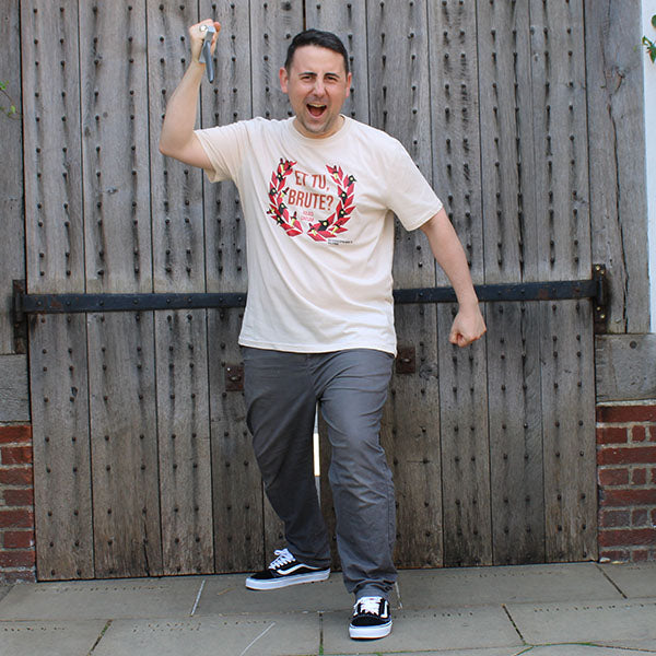 Beige t-shirt with centre front graphic of red laurel wreath with ravens and daggers within it, surrounding red graphic text