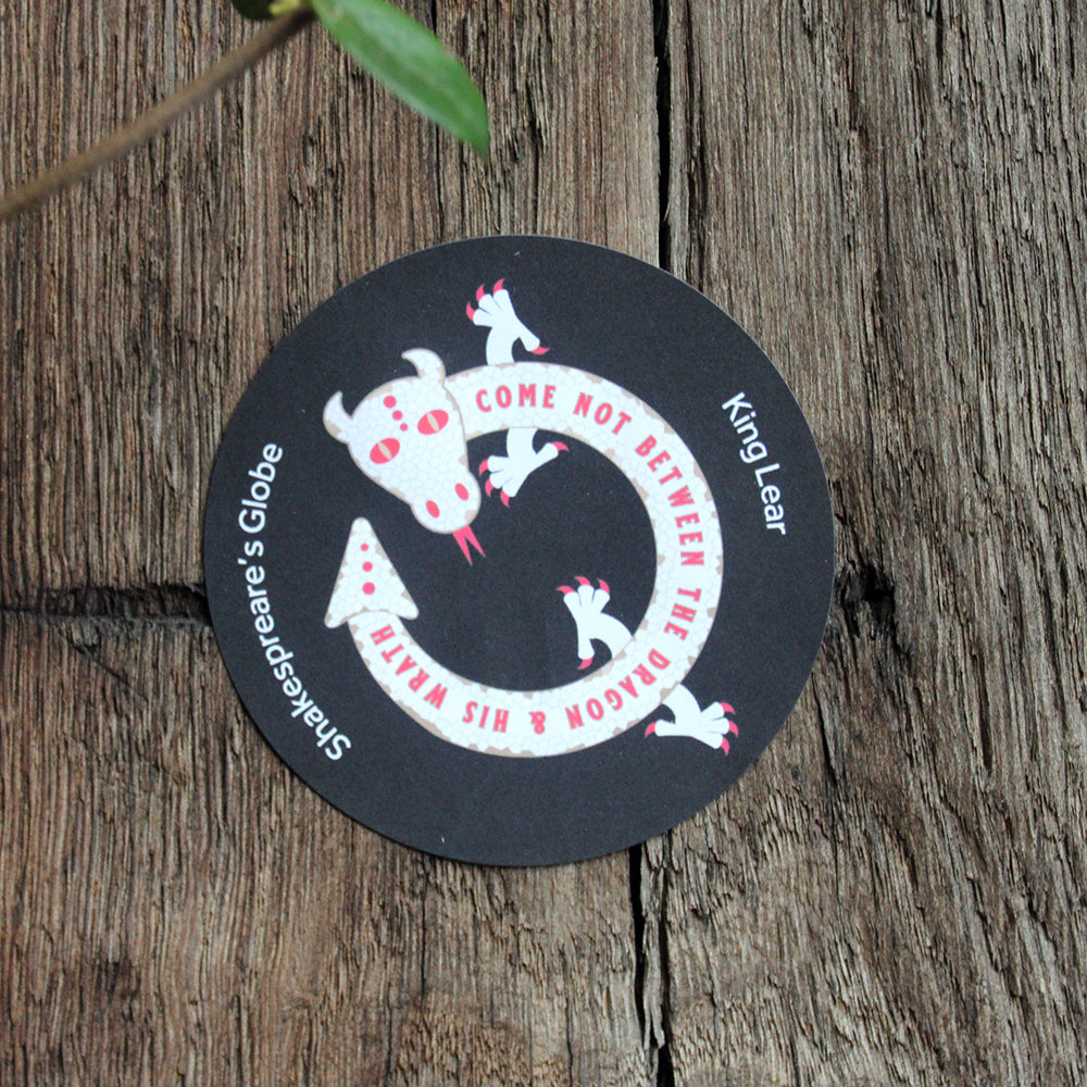 Black circular sticker with white graphic of a dragon, stuck on wood