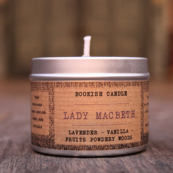 White potted candle in silver tin with tan coloured label surround with old time black print