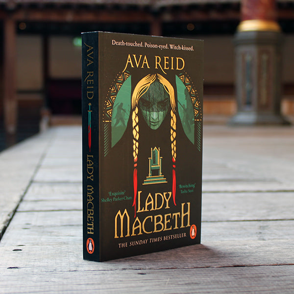 Black paperback book with image of woman's face on front cover, with long blonde braids dipped in blood, with gold text