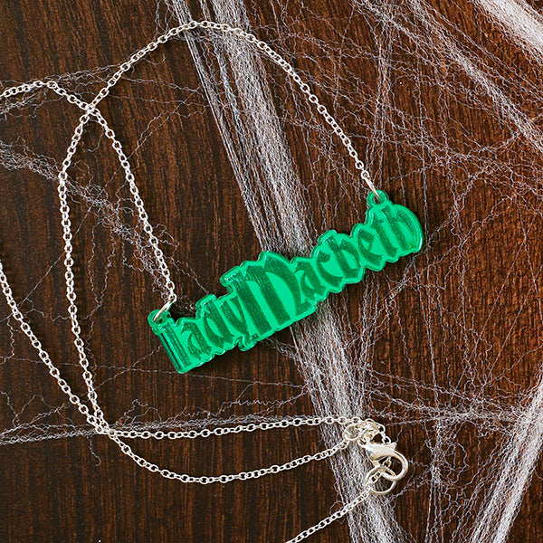 Green necklace with 'Lady Macbeth' pendant on a wooden surface