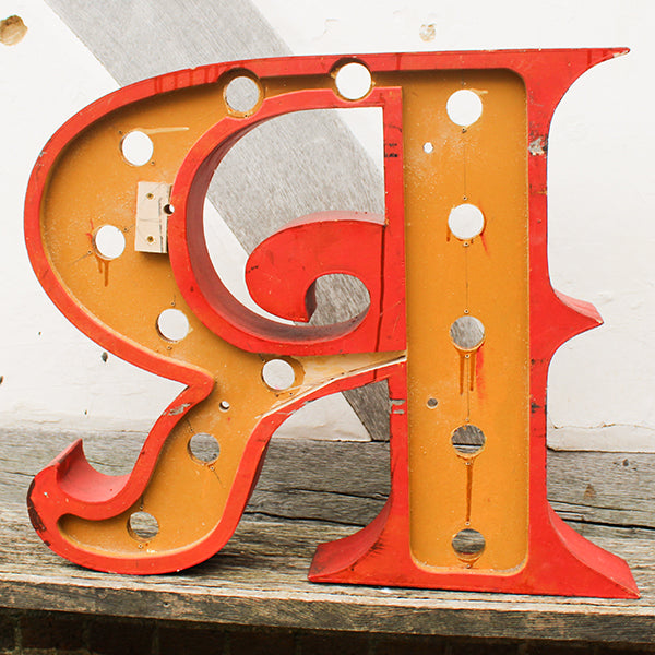 Vintage-style wooden letter 'R' with red and yellow colours on a wooden surface.