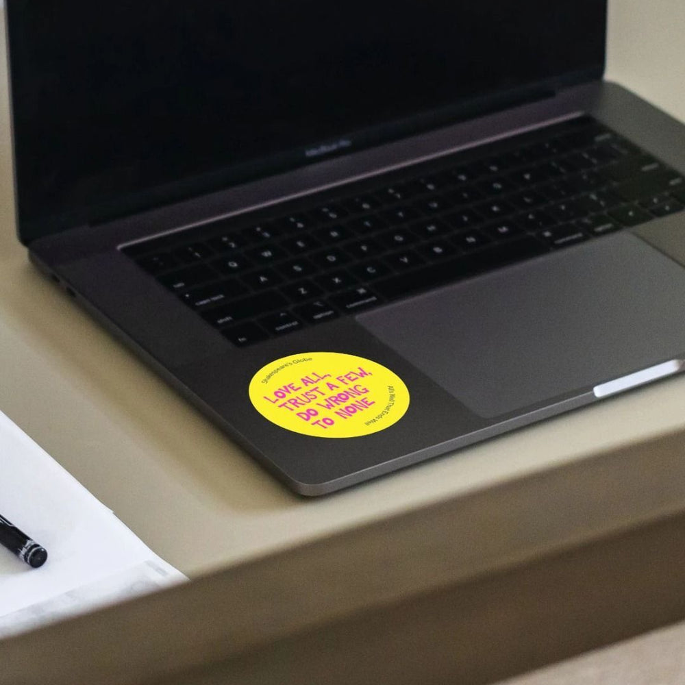 Yellow circular sticker with hot pink graphic text all over print, stuck on laptop