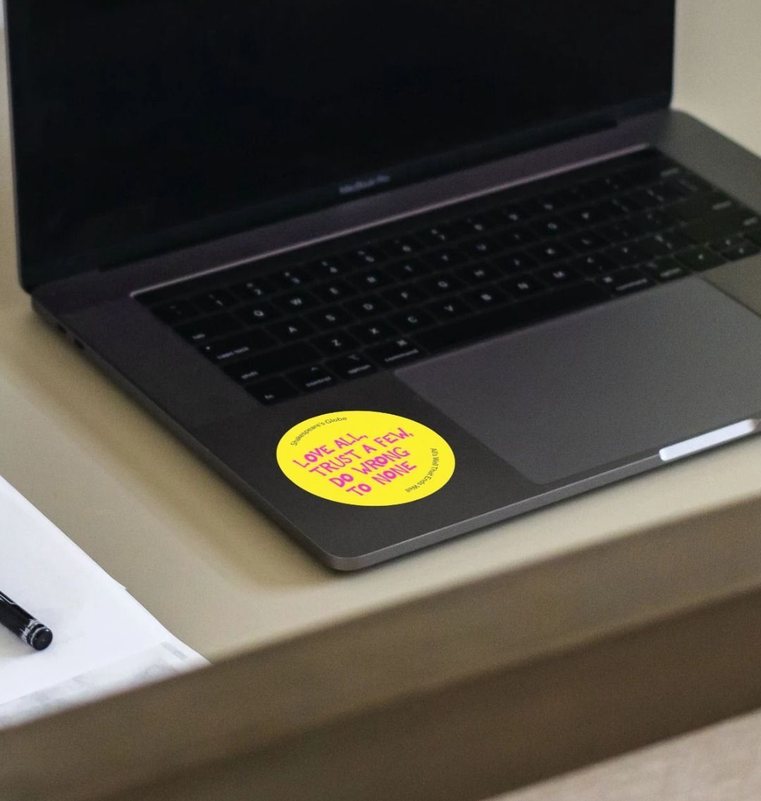 Yellow circular sticker with hot pink graphic text all over print, stuck on laptop