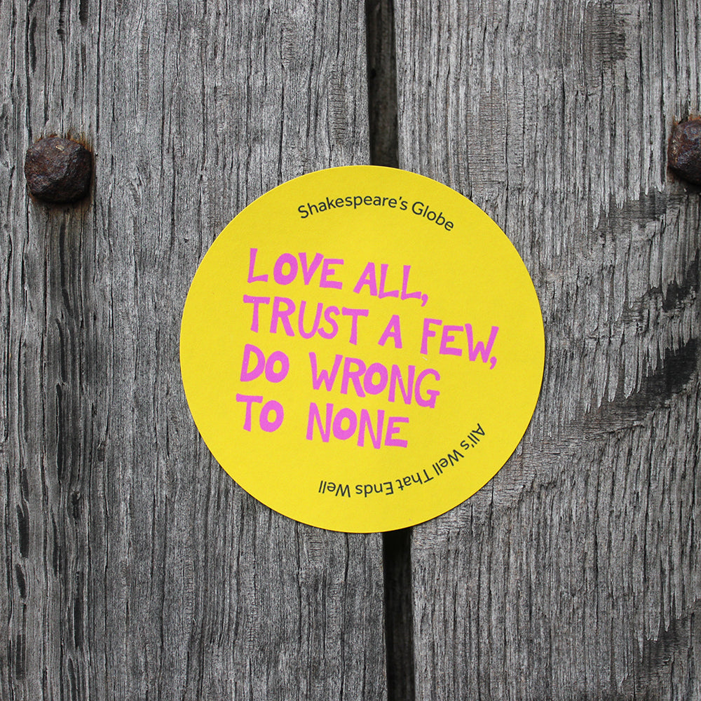 Yellow circular sticker with hot pink graphic text all over print, stuck on wood