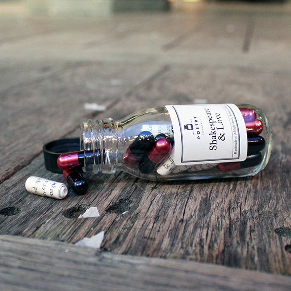 Small glass bottle with white sticker label with black text, filled with white and magenta and black pills.