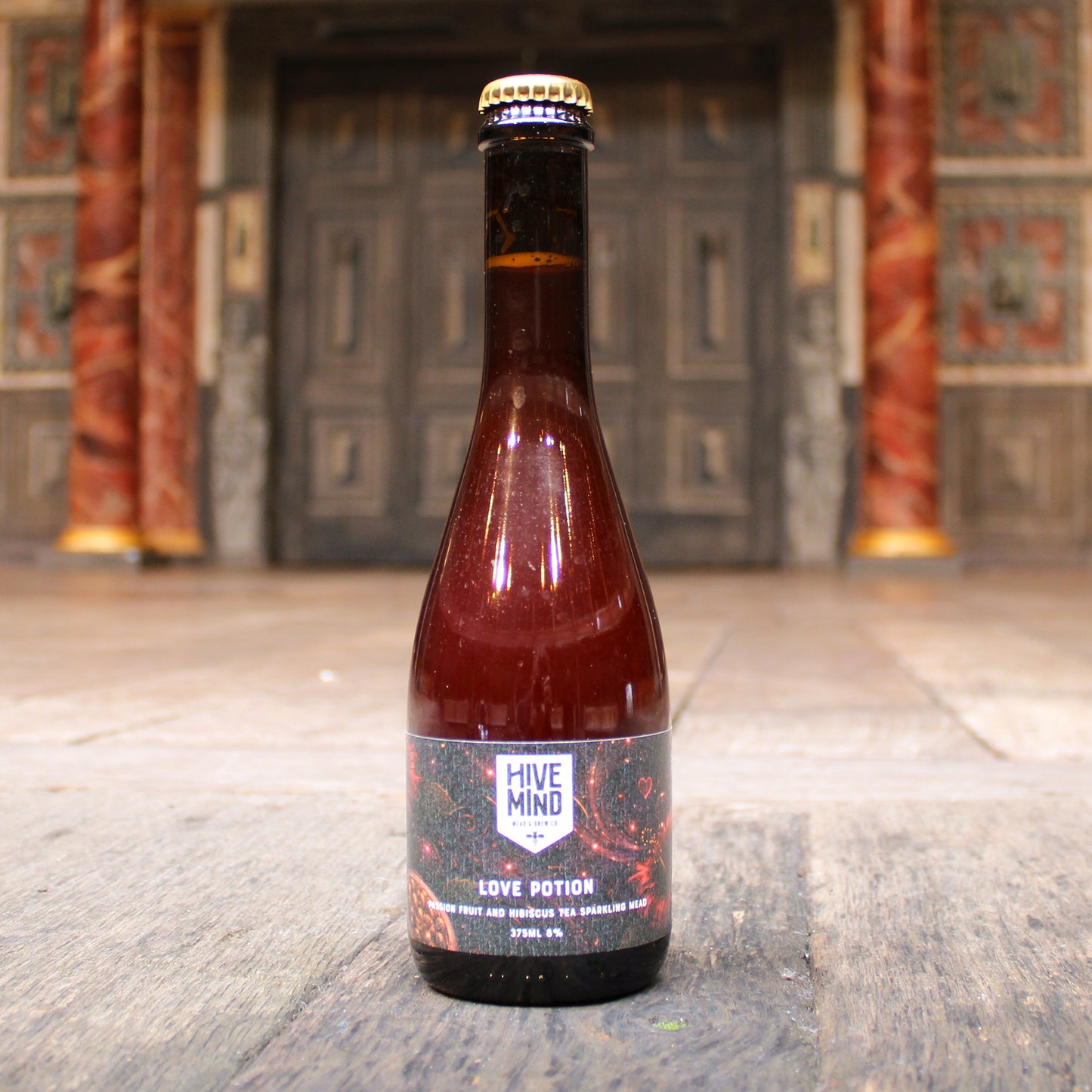 Bottle of 'Hive Mind Love Potion' on a wooden surface with a decorative background