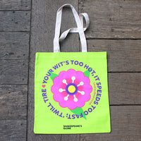 Green tote bag with a colorful flower design and text on a wooden surface