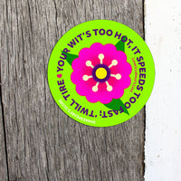 Circular sticker with a pink flower and green border on wooden surface