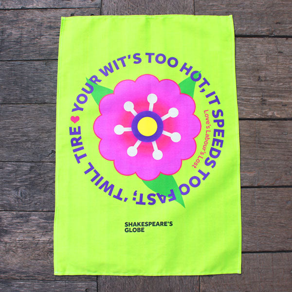 bright green tea towel printed with a large pink flower on a wooden surface