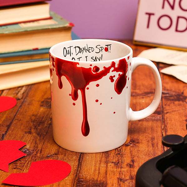 Mug with red liquid spill design on a wooden surface with books and leaves.
