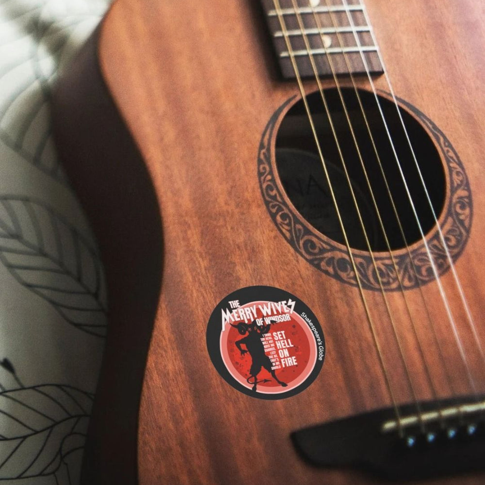 Black circular sticker with red devil graphic with white text, on a guitar