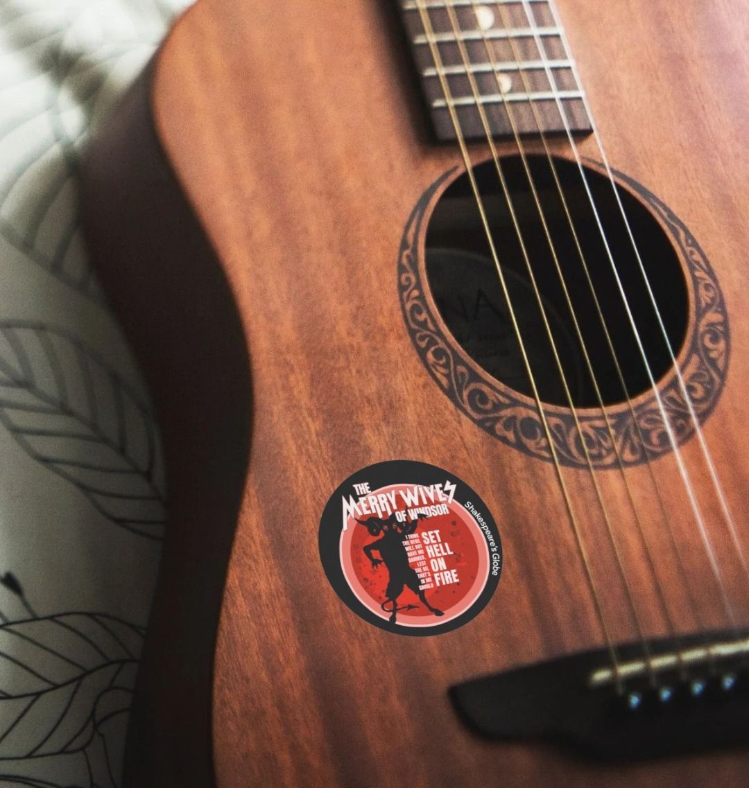 Black circular sticker with red devil graphic with white text, on a guitar