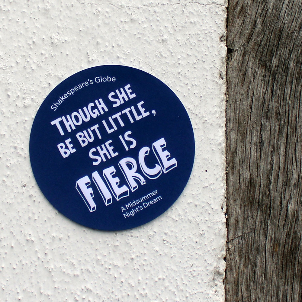 Navy blue circular sticker with white graphic text all over, stuck to a white textured wall
