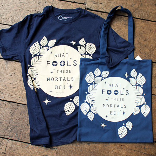 Navy blue t-shirt and tote bag with 'What Fools These Mortals Be!' design on a wooden surface