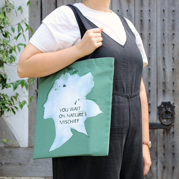 
                  
                    Green bag with black handles and a white print shaped like a woman's head
                  
                