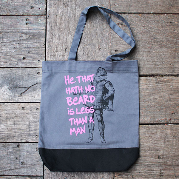 two-tone grey and black tote bag with a figure of a man and a quote in pink on a wooden surface
