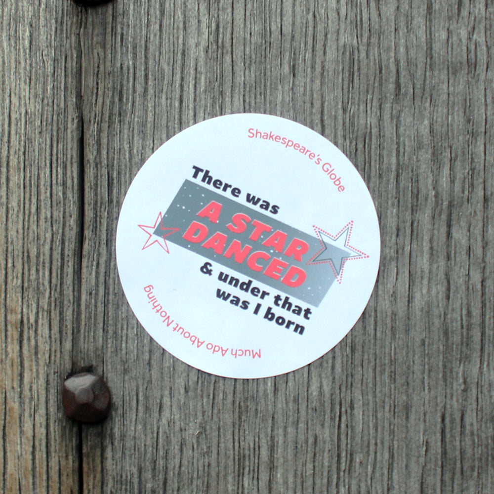 White circular sticker with 1990s style graphic text print, red and black text over gradient of grey and star designs, stuck to a wooden door
