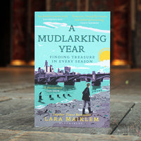 Book cover of 'A Mudlarking Year' by Lara Maiklem on a stone surface with a blurred background.
