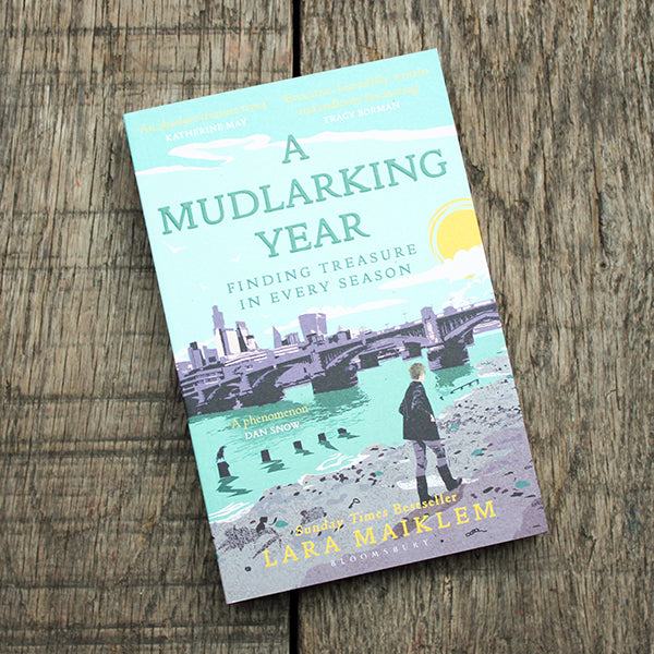 Book cover of 'A Mudlarking Year' by Lara Maiklem on a wooden surface