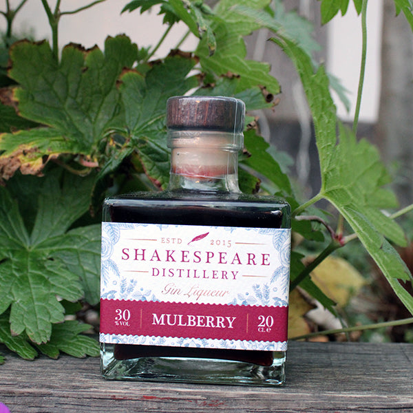 Square glass bottle with deep purple liquid inside, featuring white label with mulberry coloured writing and banner at the bottom