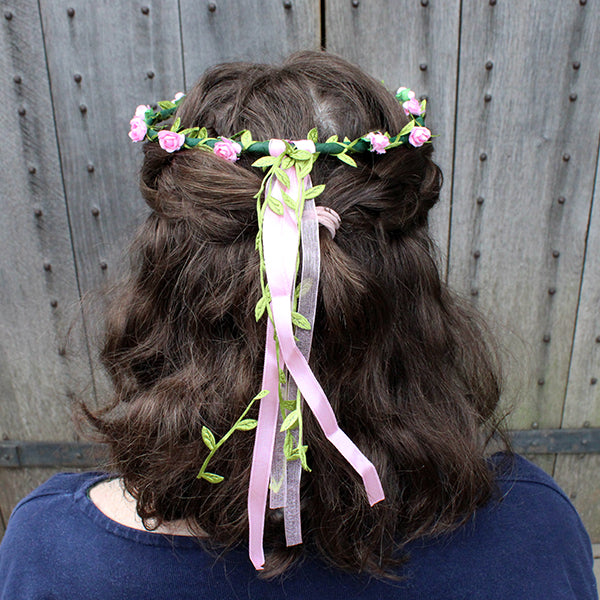 
                  
                    Faux flower, flower crown with greenery and pink flowers and ribbons on brunette shoulder length wavy hair
                  
                