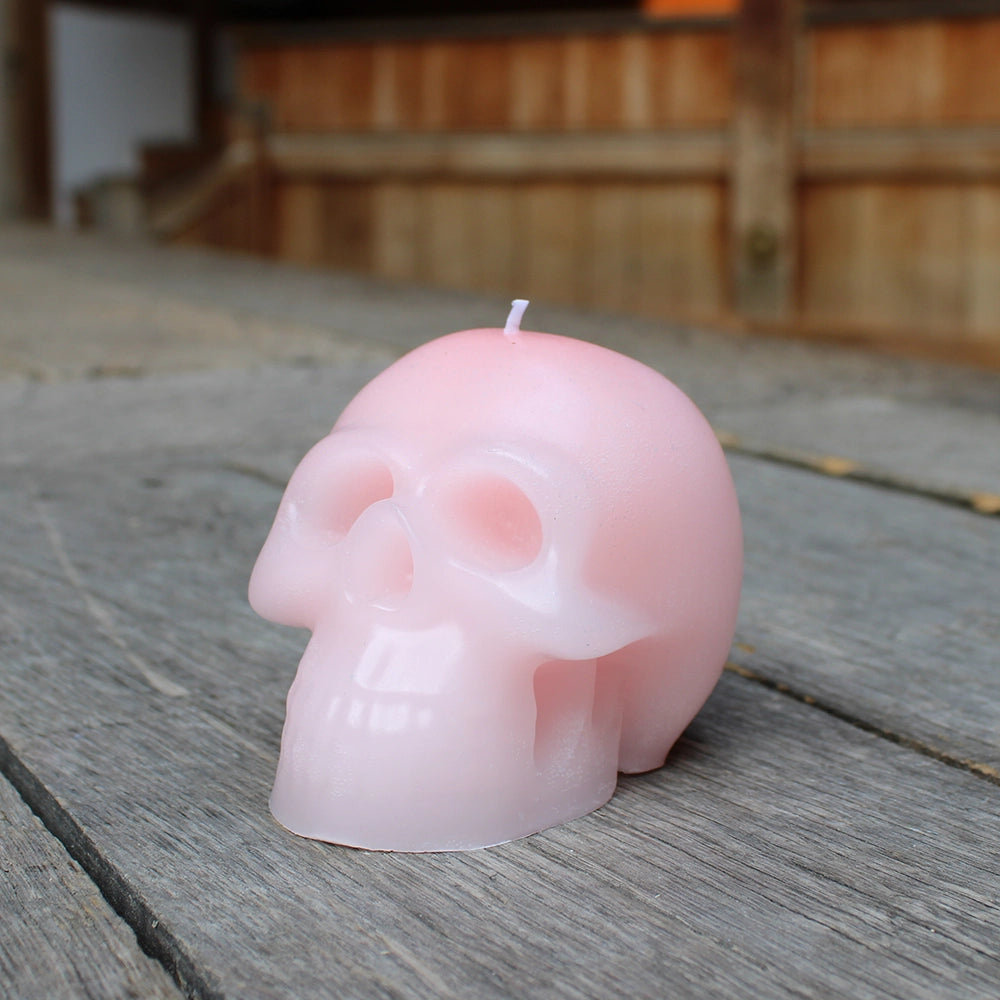 
                      
                        Pale pink skull candle with white wick, sitting on wooden stage
                      
                    