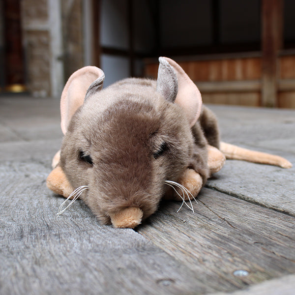 Sandy brown soft toy rat with white whiskers and beige inner ears, feet, nose and tail on wooden stage