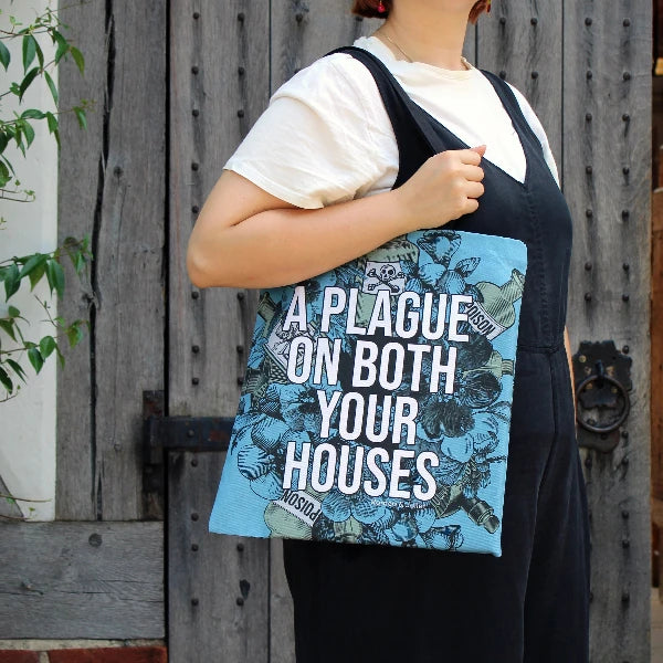 Powder blue cotton tote bag with two black handles, covered in gothic floral motif, with poison bottles, and white graphic text in centre