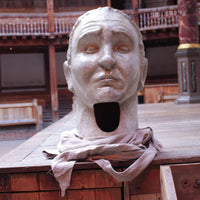 A headdress painted to look like a Roman statue with a painted face and fabric collar, displayed on the stage of the Globe Theatre