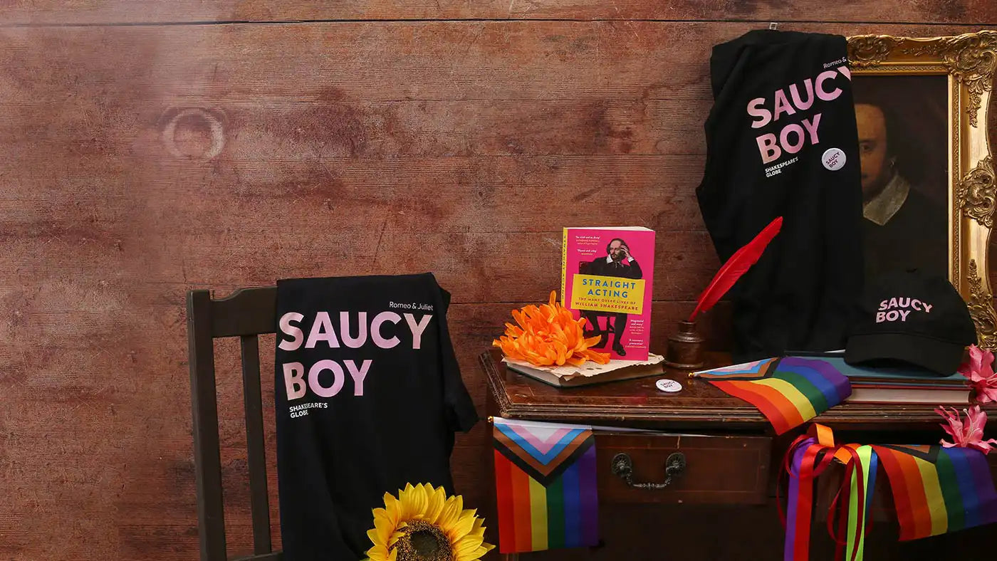Black hoodie with 'SAUCY BOY' text on a wooden surface with rainbow flags and a sunflower.