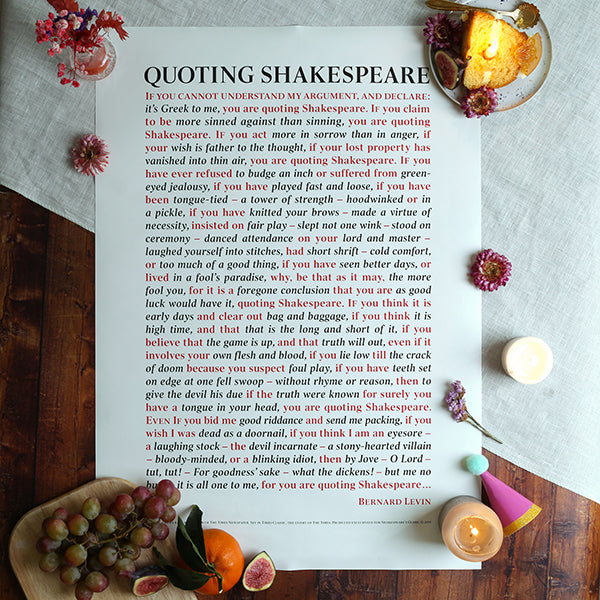 poster with text quoting Shakespeare, surrounded by candles and flowers on a wooden surface.