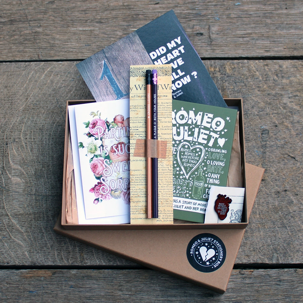 
                  
                    A kraft box containing pencils on a backing card, a green journal with white print, a blood red pin badge, a purple and brown print and a floral greetings card
                  
                