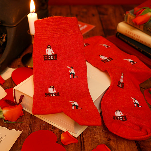 Red socks with embroidered designs on a wooden surface with books and roses.