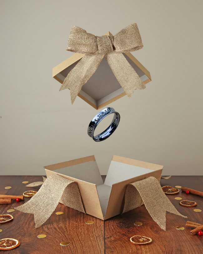 Silver engraved ring popping out of kraft box with bow on wood base with Christmas decor