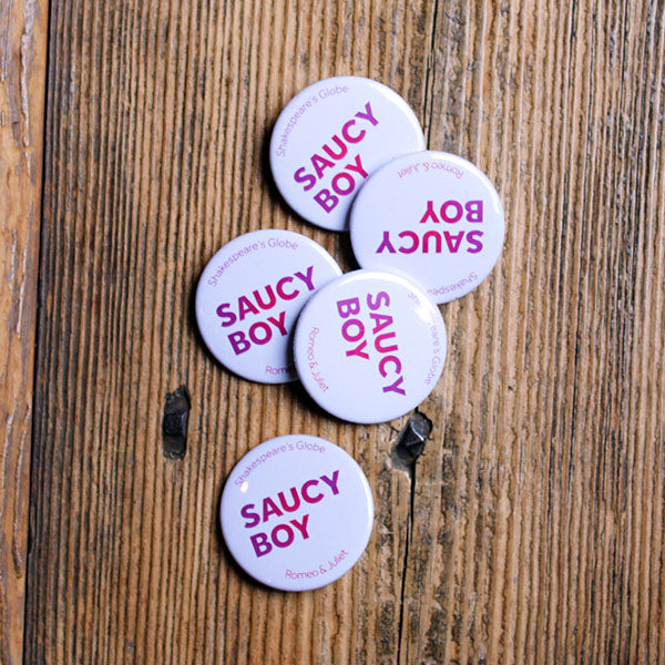 white button badge with purple-pink text lying on a wooden bench