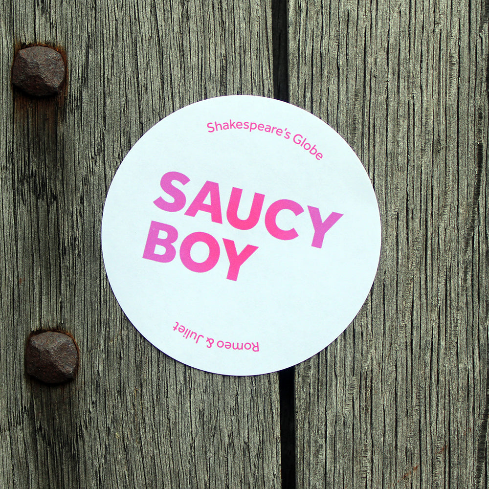 White circular sticker with gradient dark to light pink graphic text design on it, stuck on a wooden door
