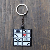 White metal key chain with a black pattern representing a half-timbered building with a red heart