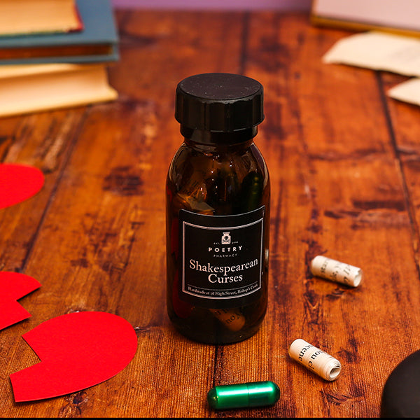 Bottle labeled 'Shakespearean Curses' on a wooden surface with heart-shaped objects and a cork.