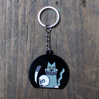 Black metal key chain with a grey cat wearing a ruff, a skull and a quill