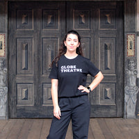 Black t-shirt with white graphic text in centre front, worn by woman with long curly brown hair standing on the Globe stage