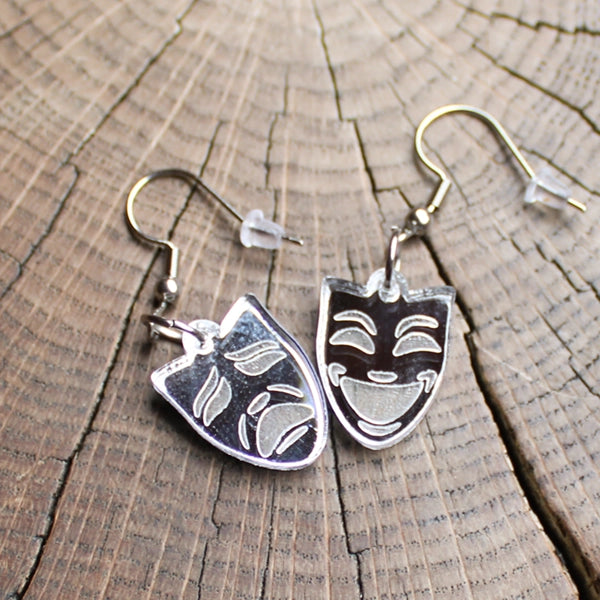 Pair of silver coloured mask-shaped earrings on a wooden surface