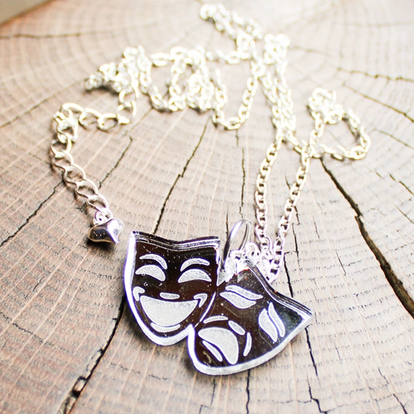 Necklace with silver coloured theatre mask pendants on a wooden surface