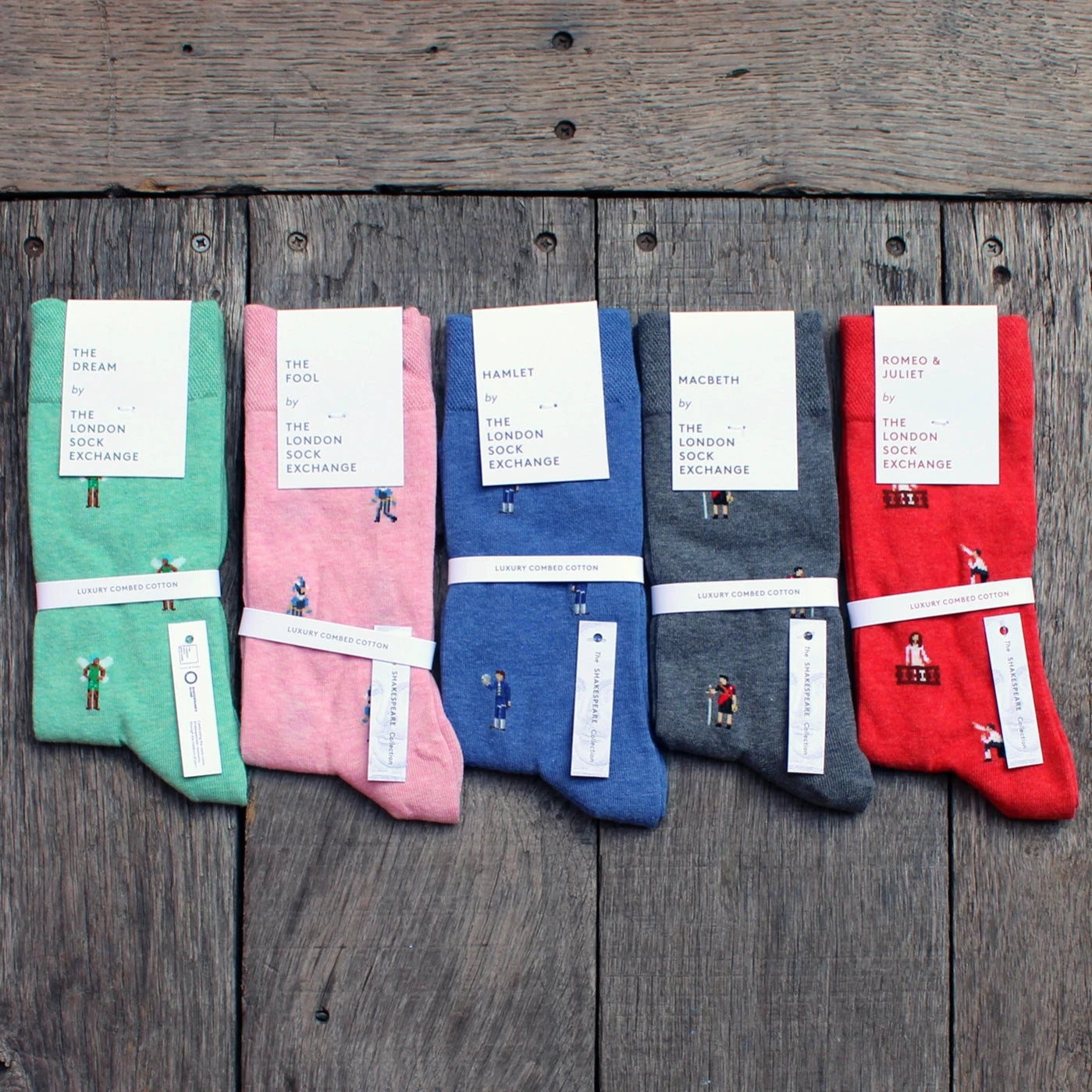 Pairs of 5 Shakespeare themed socks on wood panel stage, from left to right, teal, pink, blue, grey, red